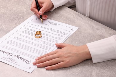 Woman signing marriage contract at light grey table, closeup