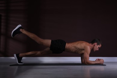 Photo of Handsome man doing plank exercise with leg lift on floor indoors