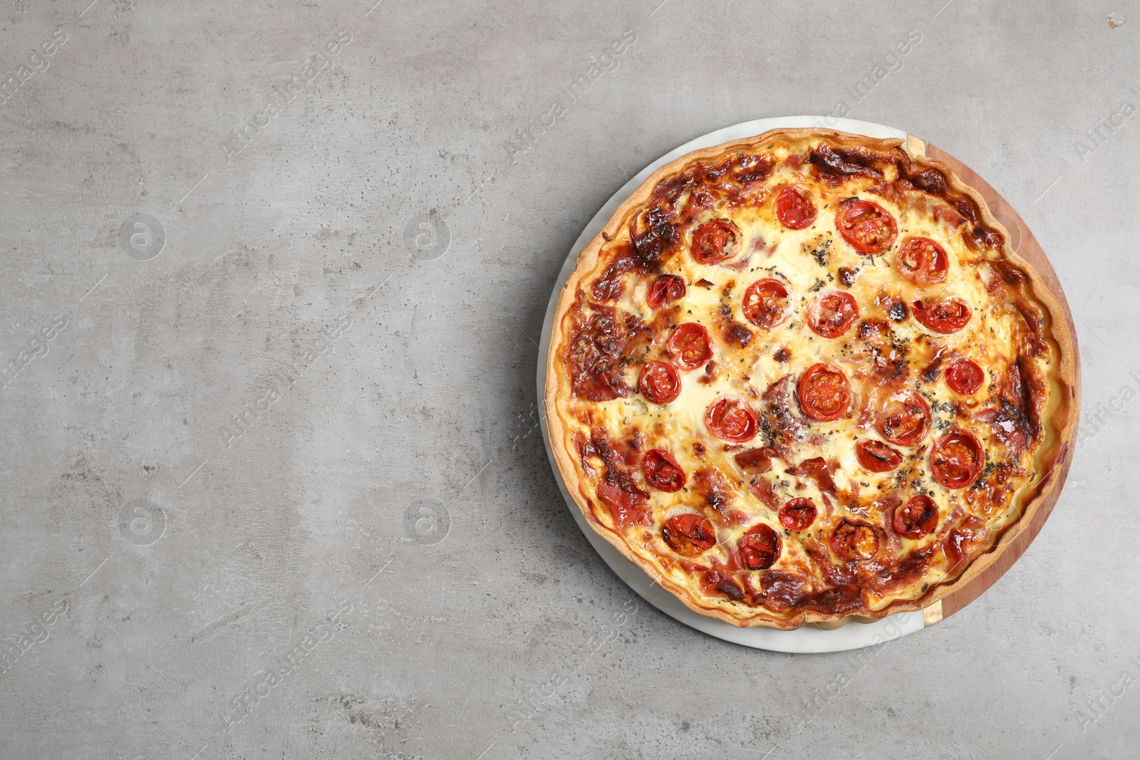 Photo of Delicious homemade quiche with prosciutto and tomatoes on light gray table, top view. Space for text