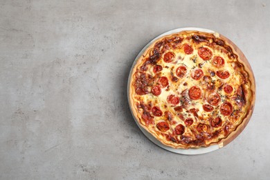 Delicious homemade quiche with prosciutto and tomatoes on light gray table, top view. Space for text