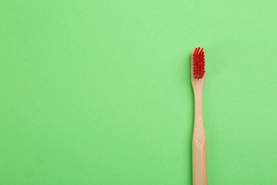 Photo of Natural bamboo toothbrush on green background, top view. Space for text