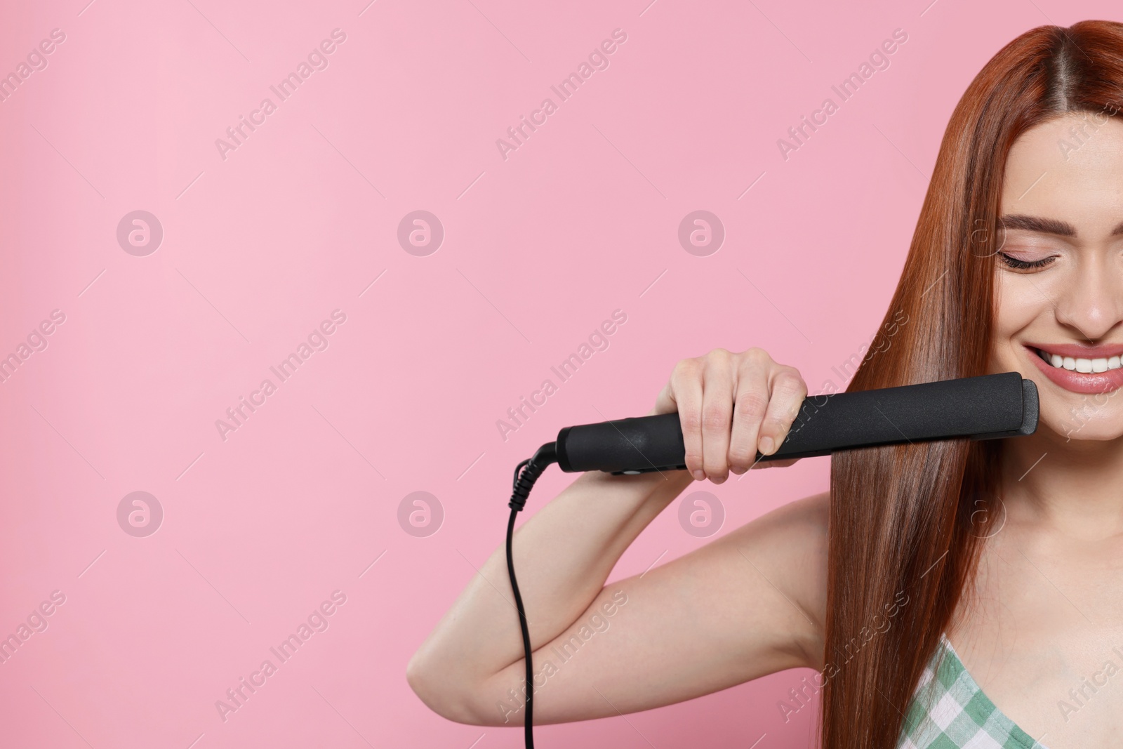 Photo of Beautiful woman using hair iron on pink background, closeup. Space for text