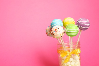 Photo of Delicious cake pops in jar full of marshmallows on color background. Space for text