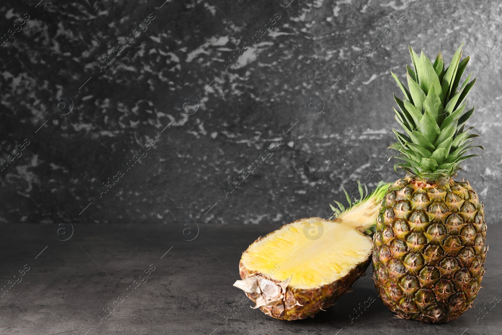 Photo of Whole and cut ripe pineapples on grey table near black wall, space for text