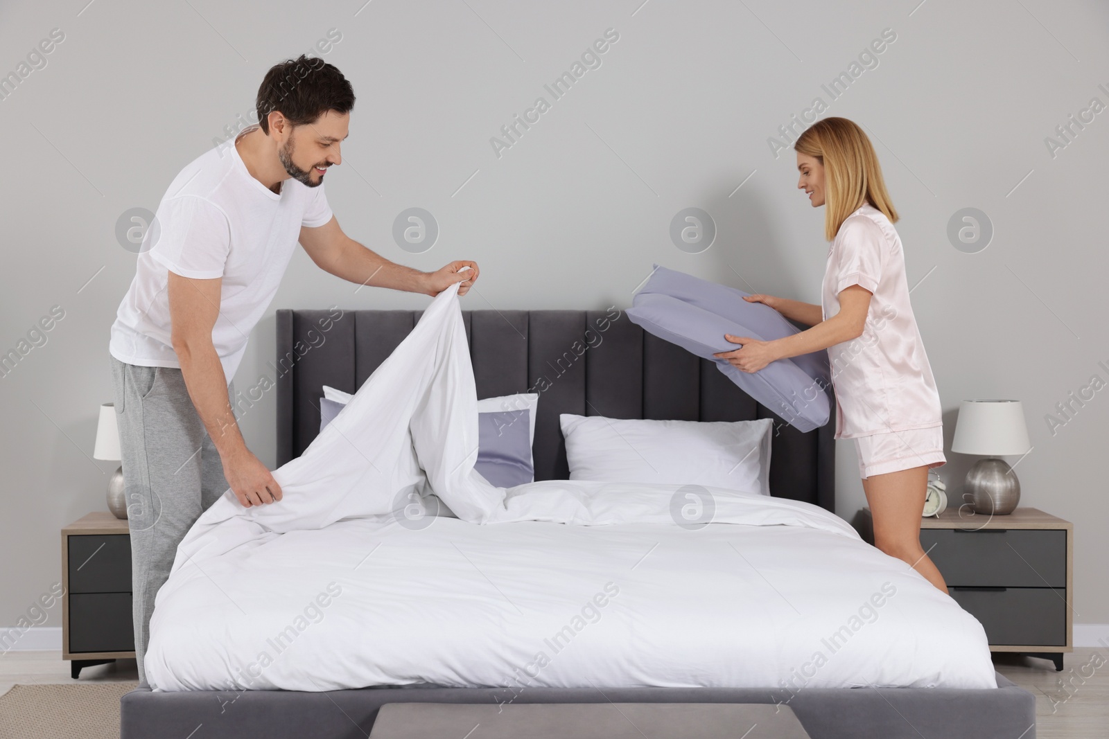 Photo of Couple changing bed linens in room. Domestic chores