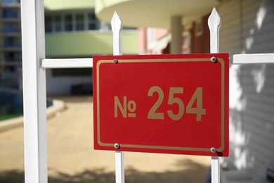 Photo of Plate with house number two hundred fifty four hanging on white iron fence outdoors, space for text