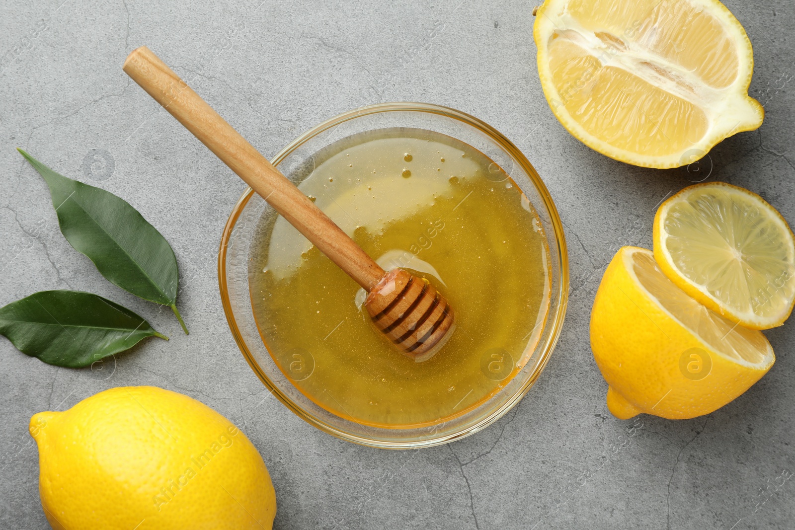 Photo of Sweet honey and fresh lemons on grey table, flat lay