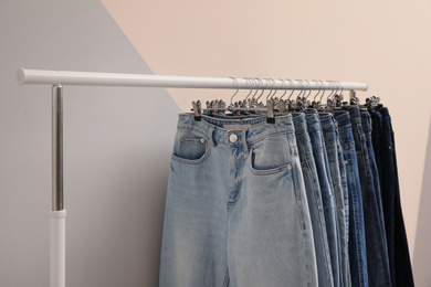 Rack with stylish jeans on color background, closeup
