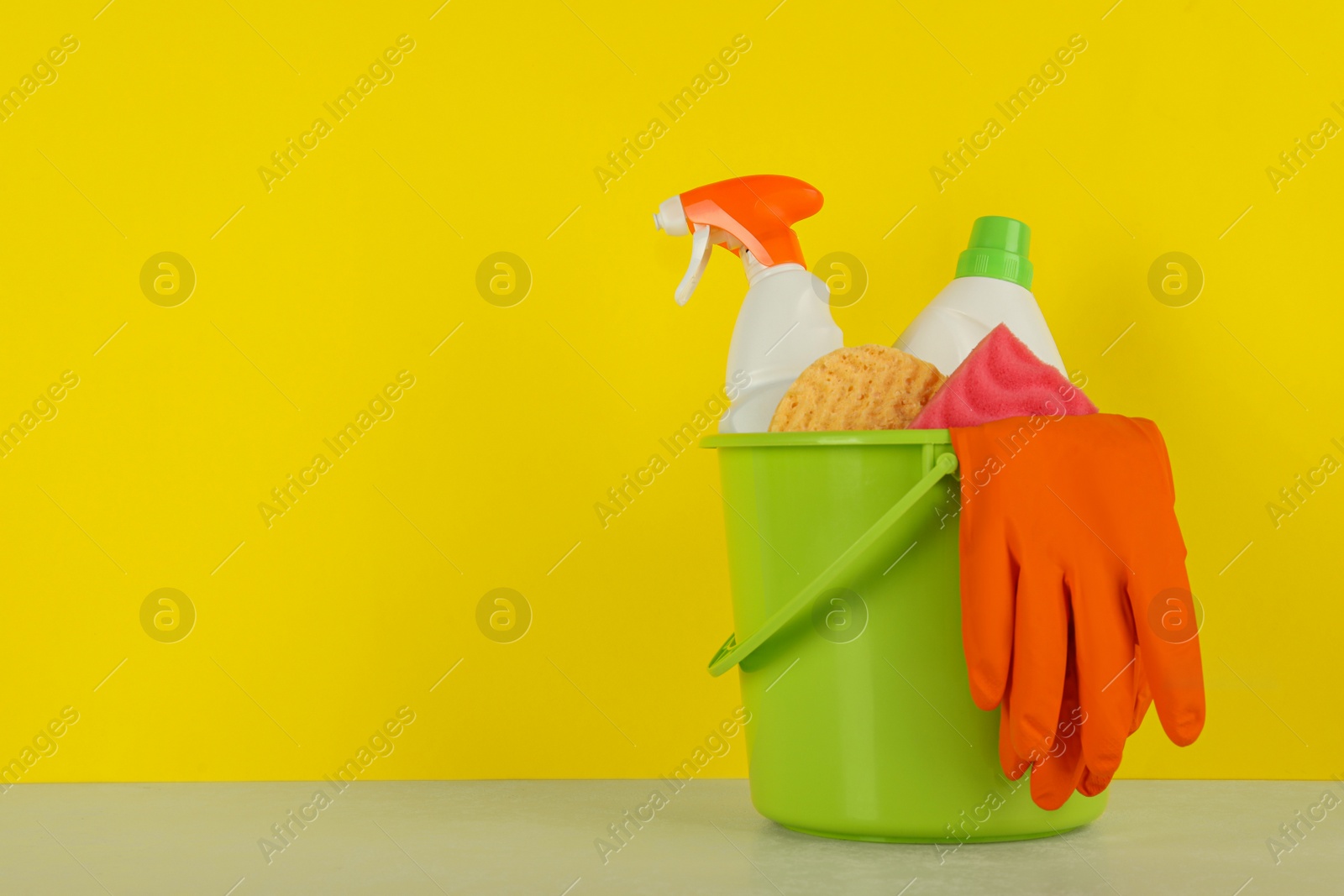 Photo of Bucket with different cleaning supplies on light floor near yellow wall. Space for text