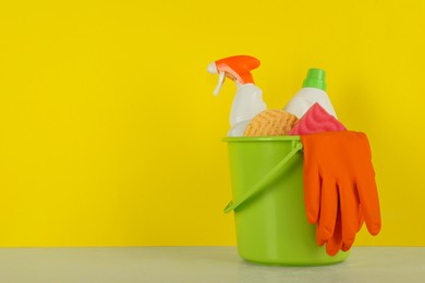 Photo of Bucket with different cleaning supplies on light floor near yellow wall. Space for text