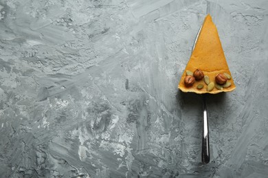 Cake server with piece of delicious pie with hazelnuts and pumpkin seeds on grey textured table, top view. Space for text