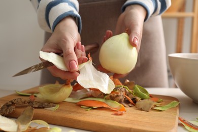 Photo of Woman peeling fresh onion with knife at white table indoors, closeup