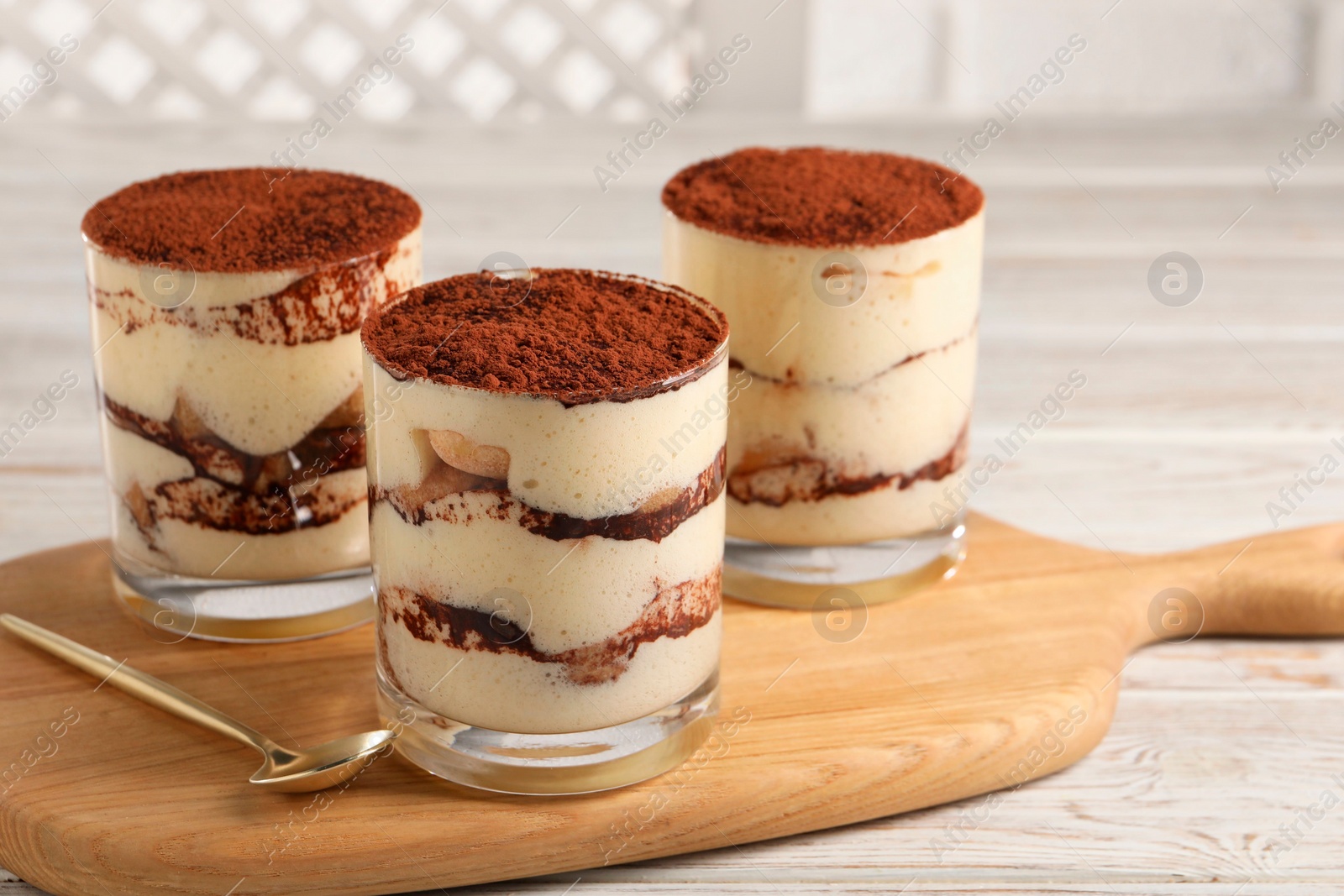 Photo of Delicious tiramisu in glasses and spoon on light wooden table, closeup