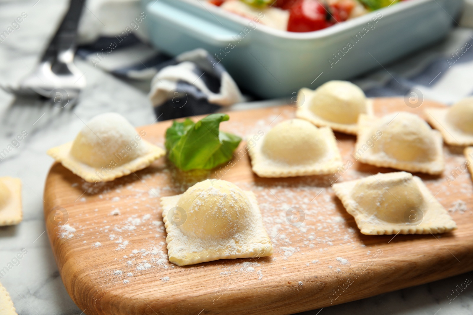 Photo of Raw ravioli with basil on wooden board, closeup