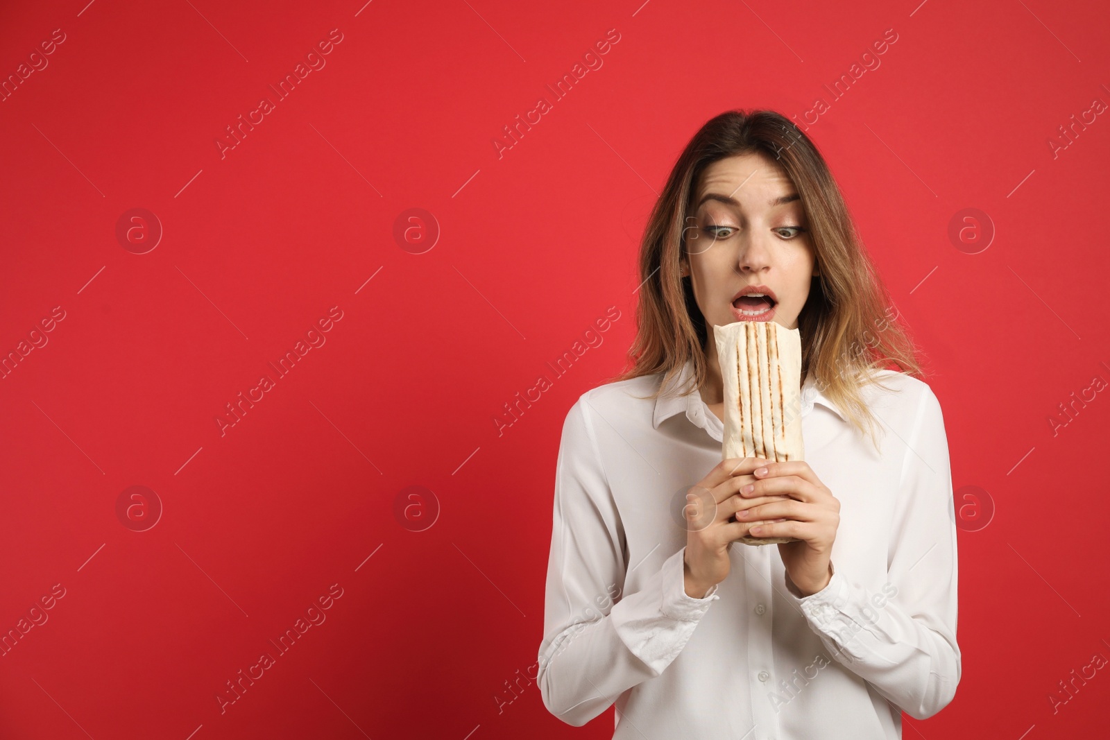 Photo of Emotional young woman with delicious shawarma on red background, space for text
