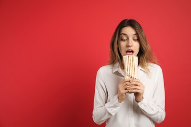 Emotional young woman with delicious shawarma on red background, space for text