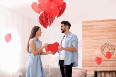 Photo of Lovely couple with heart shaped balloons in living room. Valentine's day celebration