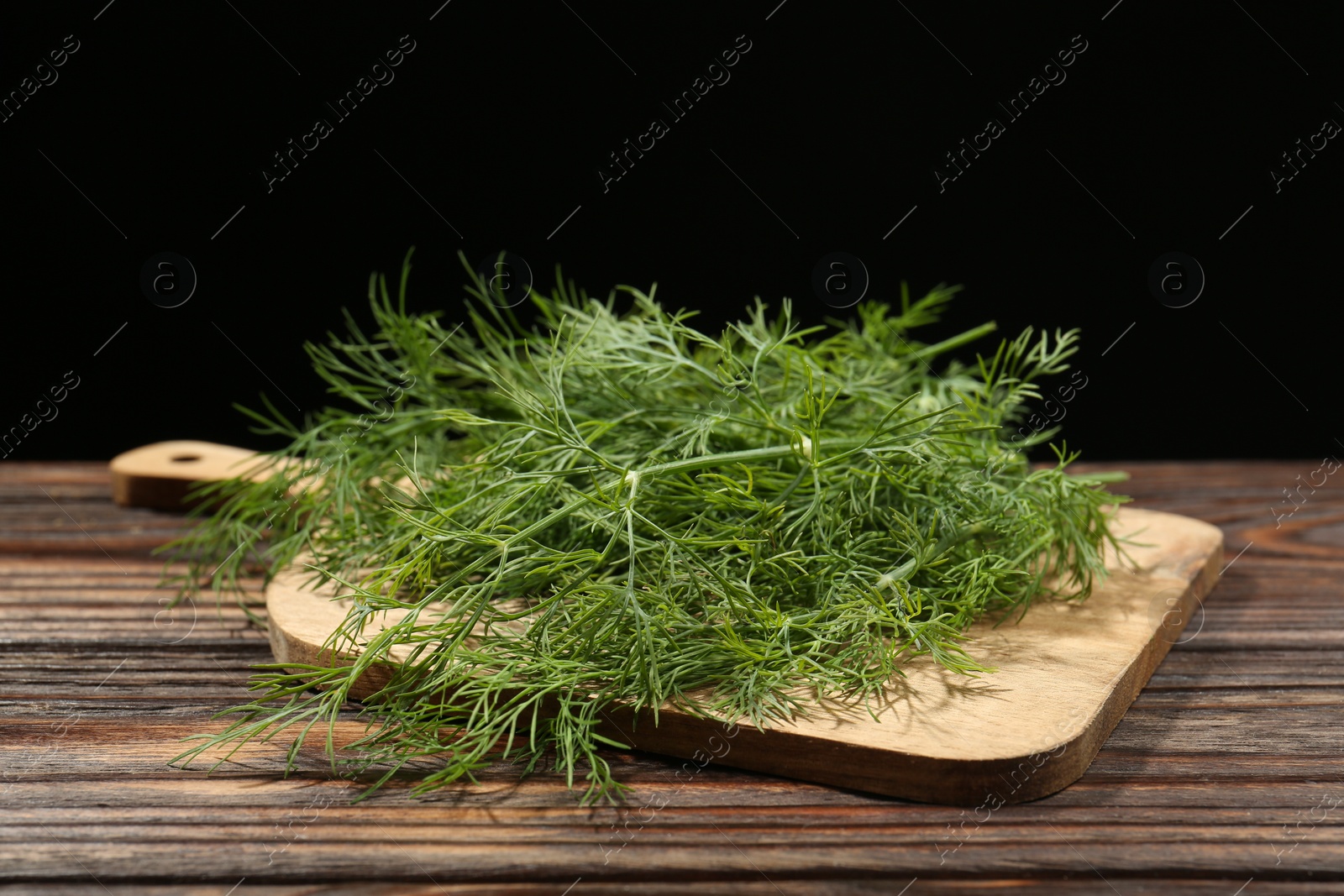 Photo of Board with fresh green dill on wooden table against black background