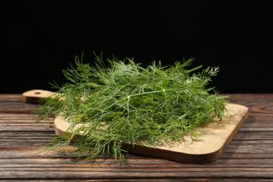 Board with fresh green dill on wooden table against black background