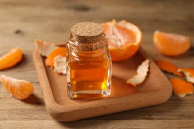 Bottle of tangerine essential oil and peeled fresh fruit on wooden table, closeup