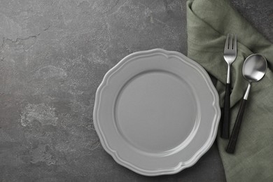 Stylish setting with cutlery, napkin and plate on grey textured table, top view. Space for text