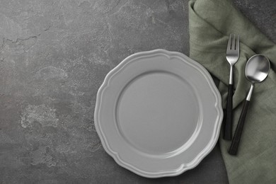 Photo of Stylish setting with cutlery, napkin and plate on grey textured table, top view. Space for text