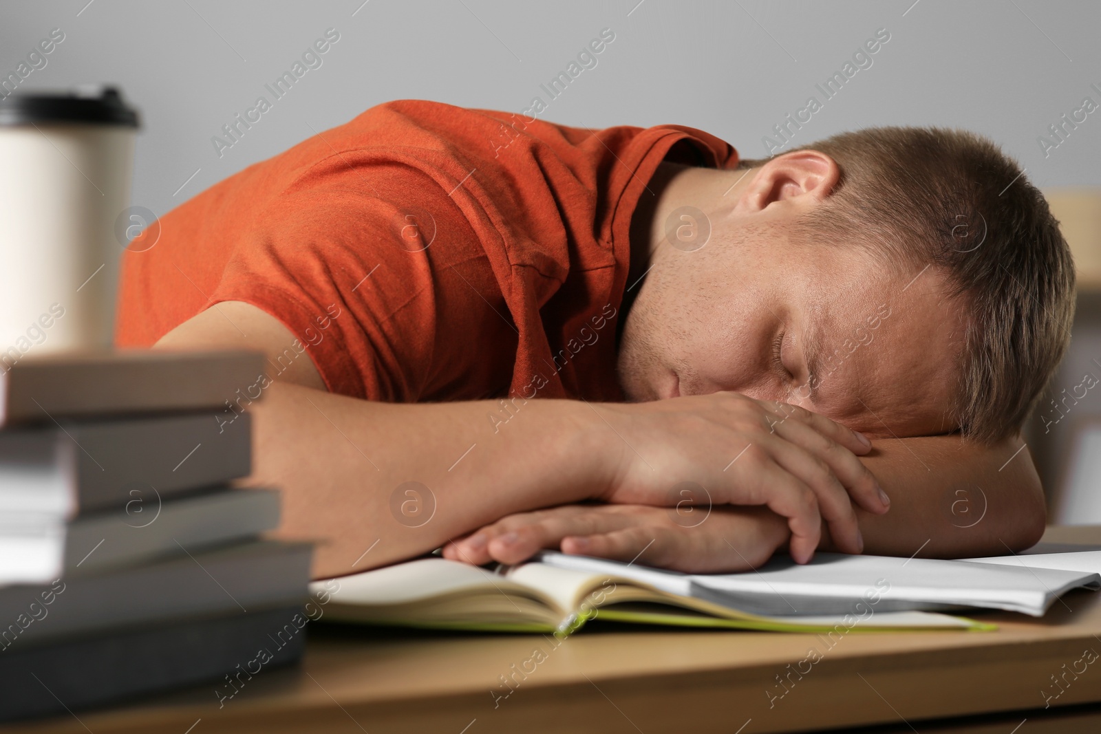 Photo of Tired man sleeping near books at wooden table indoors