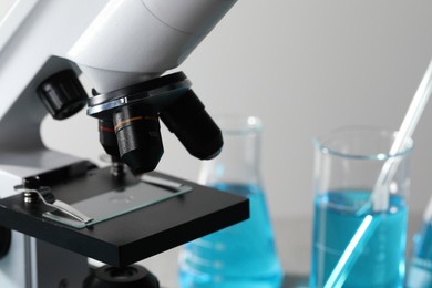 Microscope with glass slide and glassware in laboratory, closeup