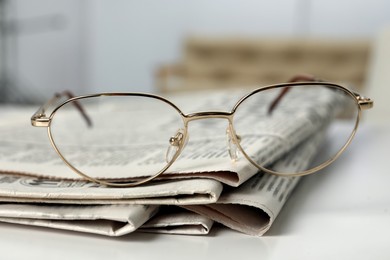 Stack of newspapers and glasses on white table indoors, closeup