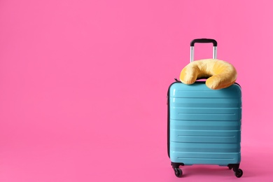 Photo of Turquoise suitcase and travel pillow on pink background, space for text