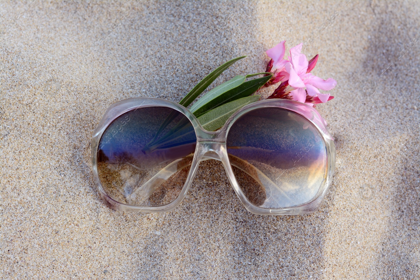 Photo of Beautiful sunglasses with tropical flower on sandy beach, top view