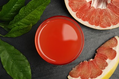 Photo of Glass of pink pomelo juice, fruit and green leaves on black table, flat lay
