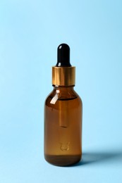 Bottle of cosmetic oil on light blue background