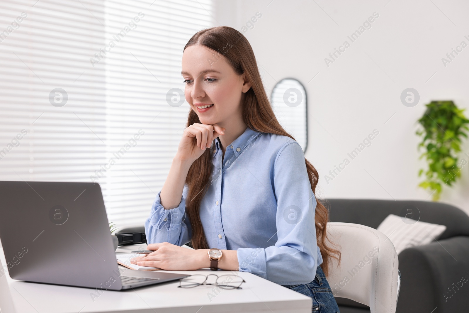 Photo of E-learning. Young woman using laptop during online lesson at white table indoors