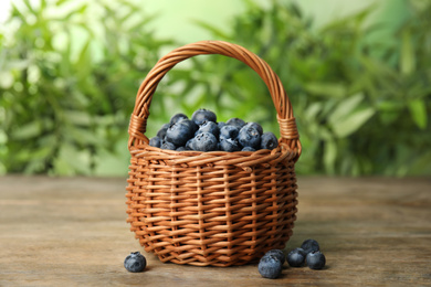 Photo of Tasty ripe blueberries in wicker basket on wooden table