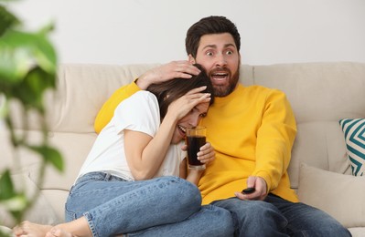 Photo of Frightened couple watching TV on sofa at home