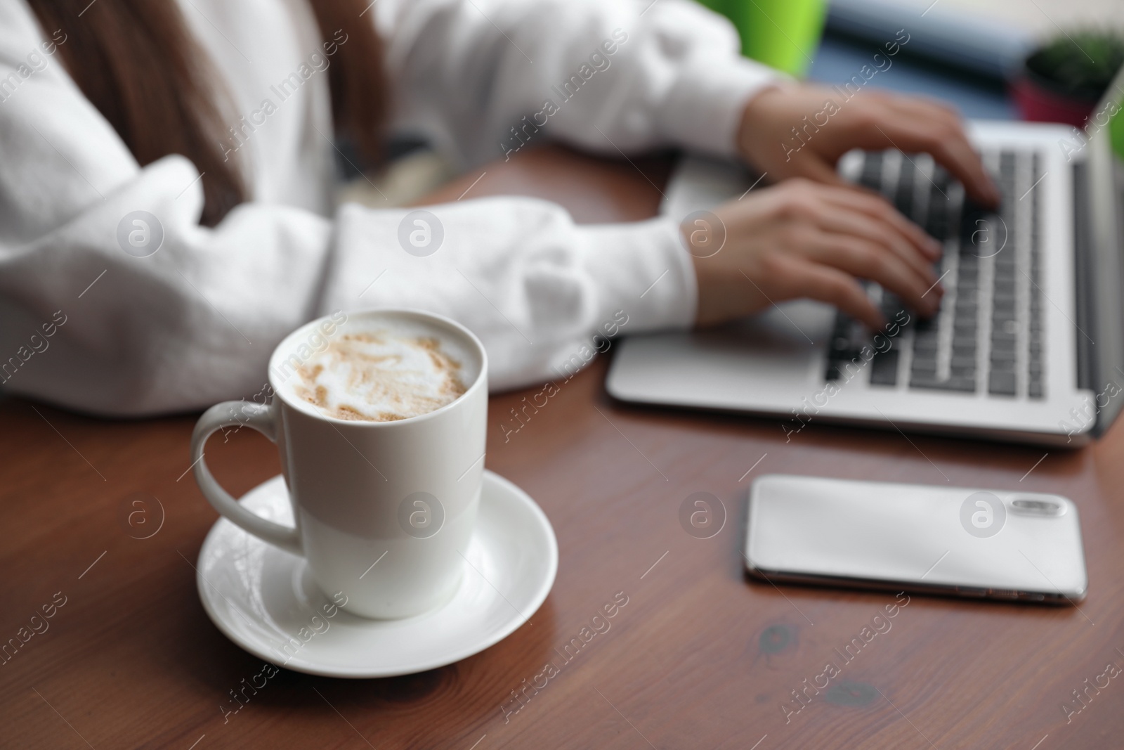 Photo of Young blogger working with laptop in cafe, focus on cup