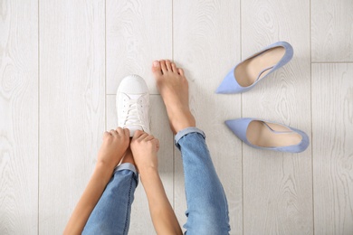 Young woman changing shoes on wooden background, top view