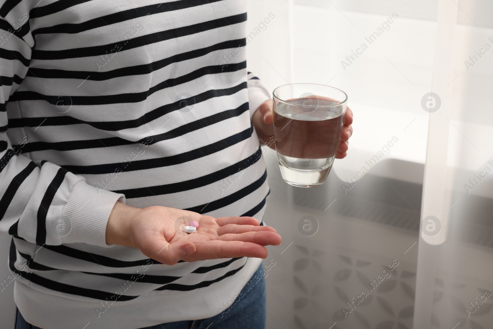 Photo of Pregnant woman with glass of water and pill at home, closeup