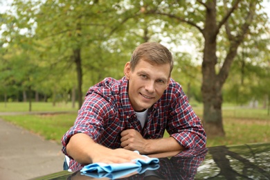 Man washing car hood with rag outdoors