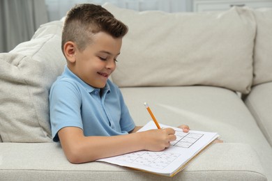 Photo of Little boy solving sudoku puzzle on sofa at home