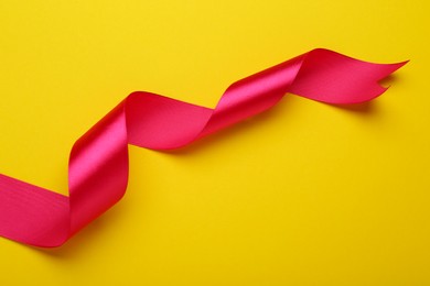 Photo of Beautiful pink ribbon on yellow background, top view. Space for text