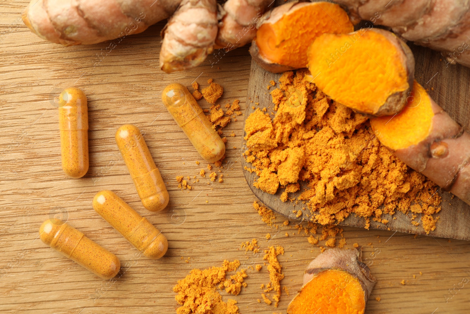 Photo of Aromatic turmeric powder, raw roots and pills on wooden table, flat lay