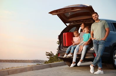 Photo of Happy young family sitting in car trunk on riverside