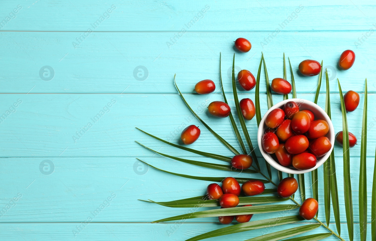 Photo of Palm oil fruits in bowl on turquoise wooden table, flat lay. Space for text