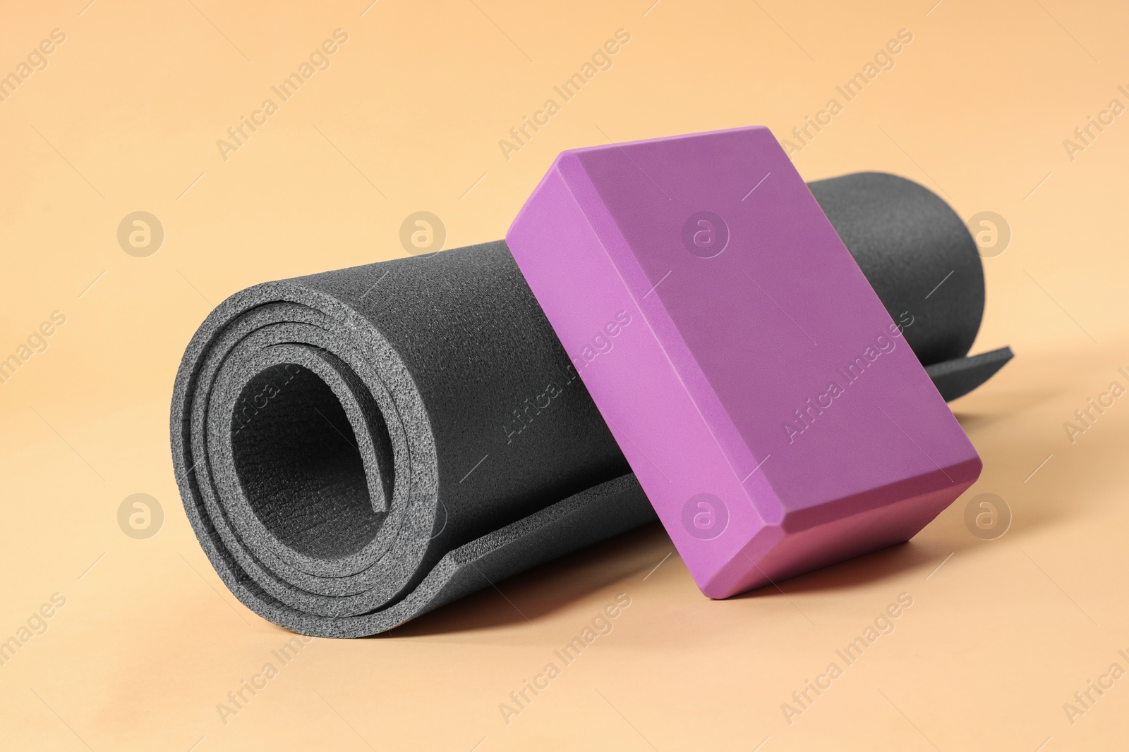 Photo of Grey exercise mat and yoga block on beige background