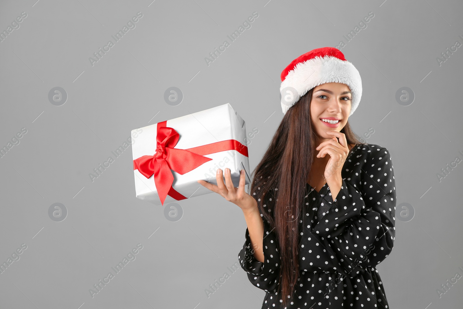 Photo of Young beautiful woman in Santa hat with gift box on grey background. Christmas celebration