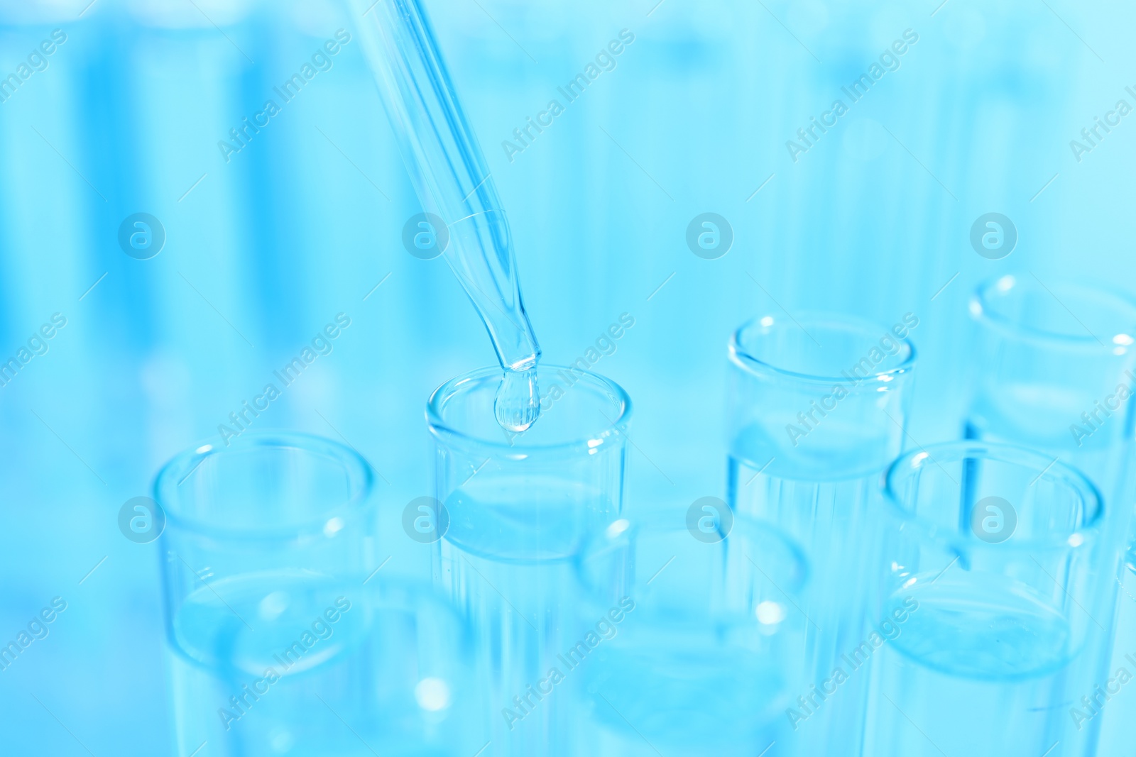 Photo of Dripping liquid from pipette into test tube on light blue background, closeup