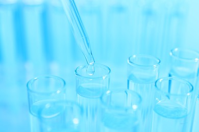 Photo of Dripping liquid from pipette into test tube on light blue background, closeup