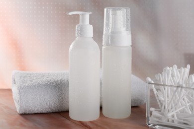 Photo of Bottles with face cleansing products, cotton buds and towel on beige marble table